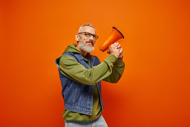 funky cheerful mature male model with beard and glasses posing with megaphone and looking at camera - Photo, Image