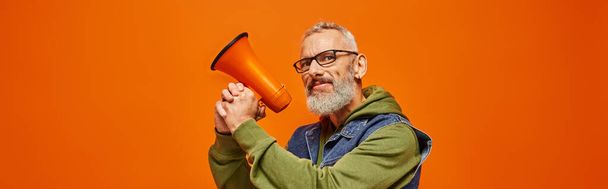 funky vrolijke volwassen man met baard en bril poseren met megafoon en kijken naar camera, banner - Foto, afbeelding
