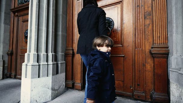 Moeder en kind hand in hand lopen in de religieuze tempel reikend naar deurknop en openen naar houten traditionele deur - Foto, afbeelding
