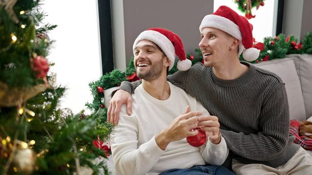 Двое мужчин празднуют Рождество украшая елку дома - Фото, изображение