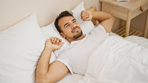 Молодий іспаномовний чоловік прокидається розтягуючи руки в спальні
 - Фото, зображення