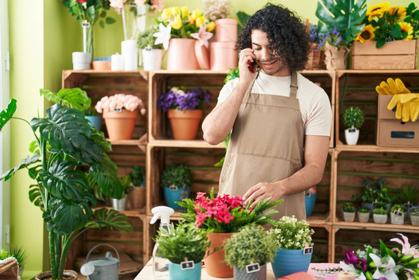 Молодий латинський чоловік флорист посміхається впевнено розмовляючи на смартфоні в квітковому магазині - Фото, зображення