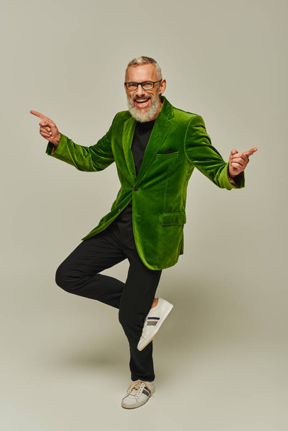 beau gai mature homme dans vibrant vert blazer posant sur une jambe et souriant à la caméra - Photo, image