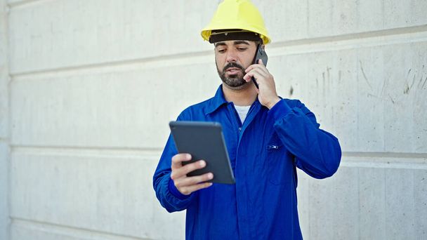 Fiatal spanyol férfi dolgozó beszél okostelefonon segítségével touchpad az építkezésen - Fotó, kép