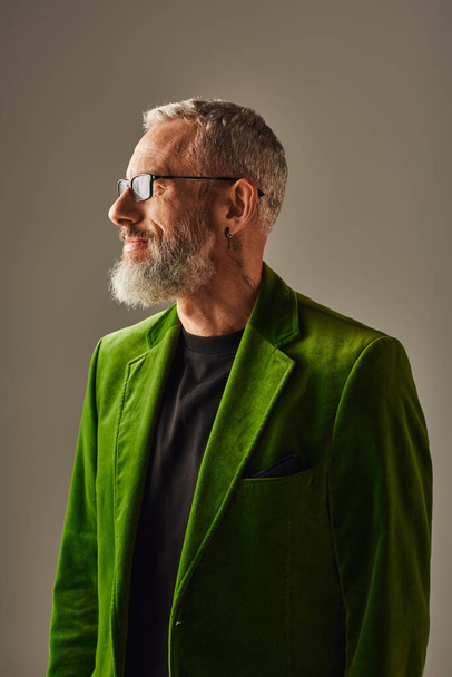 fröhlich gutaussehendes männliches Modell in grünem, lebendigem Blazer mit grauem Bart und Brille, die wegschaut - Foto, Bild