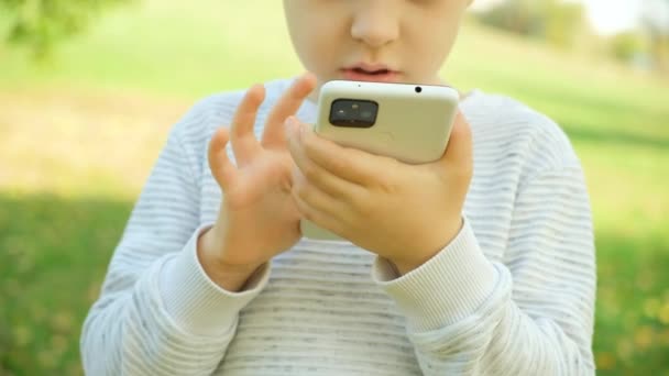 Niño pequeño usando el teléfono inteligente al aire libre, manos de cerca. - Metraje, vídeo