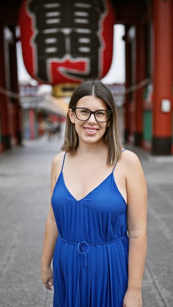 Belle femme hispanique portant des lunettes, exhibant un sourire joyeux au temple senso-ji, immergée dans la tradition japonaise, joyeuse adulte latino explorant la riche culture de tokyo - Photo, image