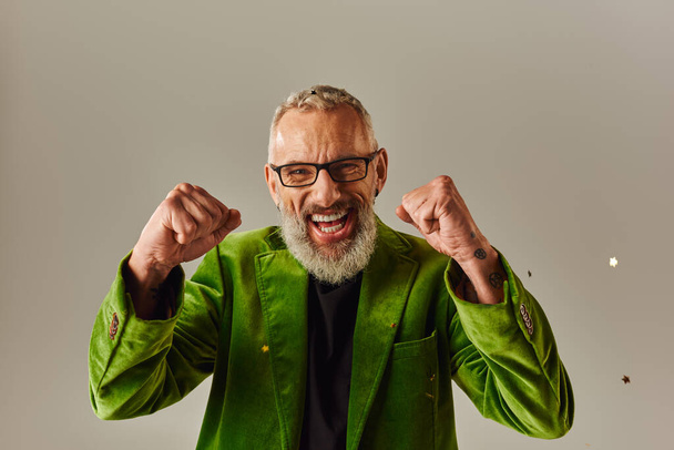 cheerful handsome mature man in green blazer smiling and showing fists at camera on beige backdrop - Photo, Image