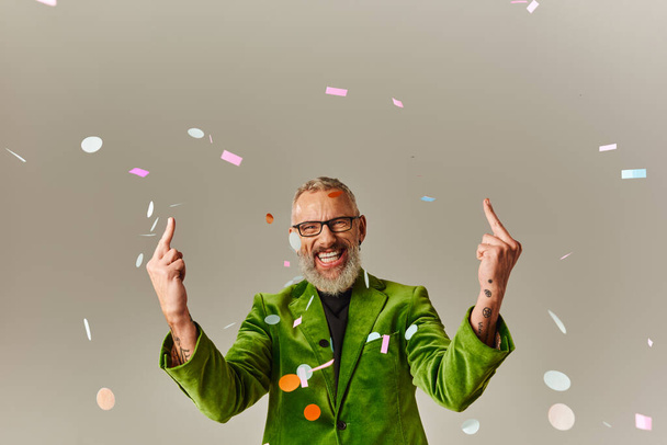 homem maduro alegre em blazer vibrante verde com óculos mostrando os dedos do meio e sorrindo para a câmera - Foto, Imagem