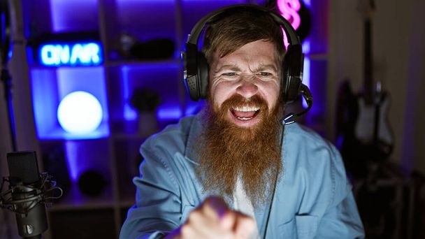 Cheerful young redhead streamer celebrates epic win. man playing video game, pointing at camera in home gaming room - Photo, image