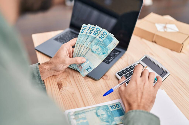 Jongeman e-commerce zakenman met Braziliaanse echte bankbiljetten boekhouding op kantoor - Foto, afbeelding