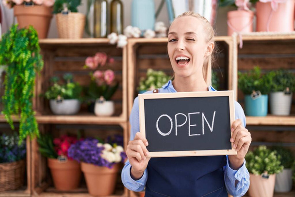 Young caucasian woman working at florist holding open sign winking looking at the camera with sexy expression, cheerful and happy face.  - Photo, Image