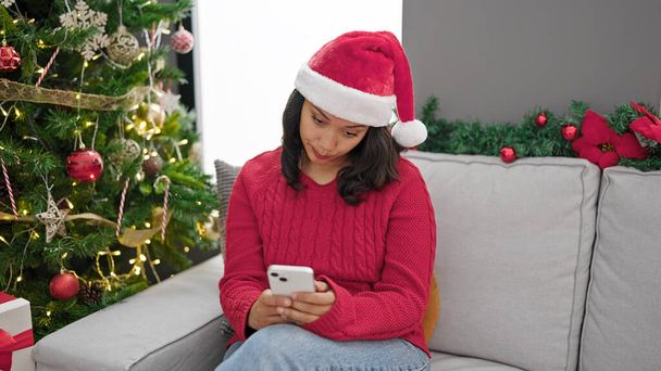 Jeune belle femme hispanique en utilisant un smartphone célébrant Noël à la maison - Photo, image