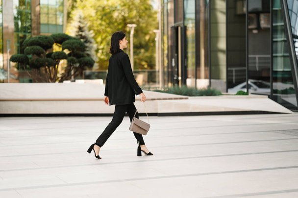 Φωτογραφία της νεαρής γυναίκας σε περιστασιακό περπάτημα στη δουλειά κοντά στο επιχειρηματικό κέντρο γραφείο. - Φωτογραφία, εικόνα
