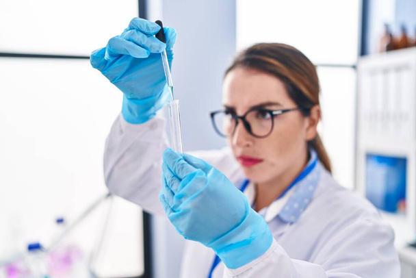 Junge schöne hispanische Wissenschaftlerin gießt im Labor Flüssigkeit ins Reagenzglas - Foto, Bild