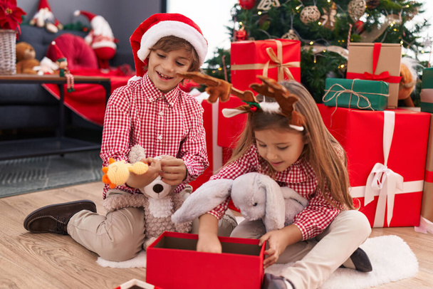 Αδελφός και αδελφή ξεπακετάρισμα δώρο κάθεται στο πάτωμα από το χριστουγεννιάτικο δέντρο στο σπίτι - Φωτογραφία, εικόνα