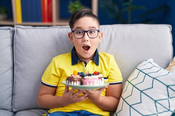 Nuori latino lapsi tilalla kakku makeisia juhlii hullu ja hämmästynyt menestystä avoimet silmät huutaa innoissaan.  - Valokuva, kuva