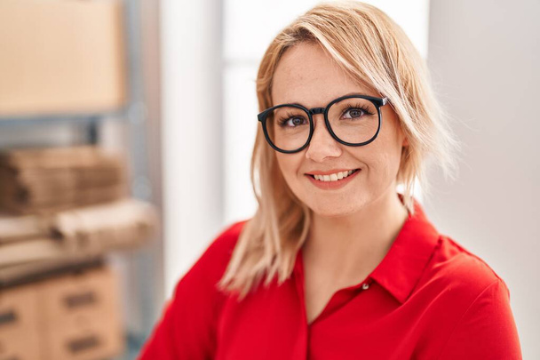 Jonge blonde vrouw e-commerce zakenman glimlachen vertrouwen op kantoor - Foto, afbeelding