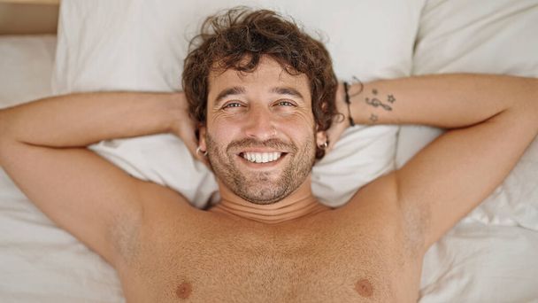 Νεαρός Ισπανός χαλαρός στο κρεβάτι χαμογελώντας γυμνός στην κρεβατοκάμαρα. - Φωτογραφία, εικόνα