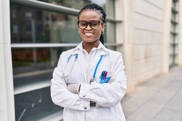 Африканская американка доктор улыбается уверенно стоя со скрещенными руками в больнице - Фото, изображение