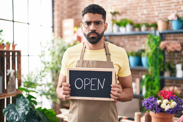 Hispanic man with beard working at florist holding open sign skeptic and nervous, frowning upset because of problem. negative person.  - Photo, Image