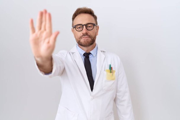 Middle age doctor man with beard wearing white coat doing stop sing with palm of the hand. warning expression with negative and serious gesture on the face.  - Photo, Image