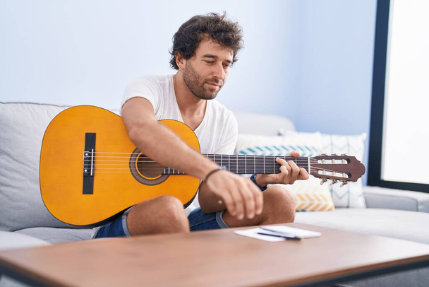 Молодий іспаномовний чоловік грає на класичній гітарі, що складає пісню вдома
 - Фото, зображення