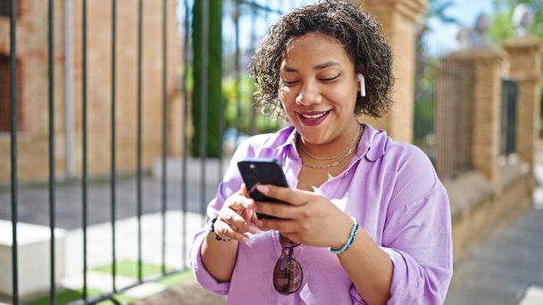 Młoda piękna latynoska kobieta za pomocą smartfona i słuchawek na ulicy - Zdjęcie, obraz