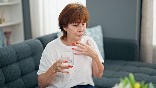 Frau mittleren Alters trinkt Glas Wasser und hustet nach Hause - Foto, Bild