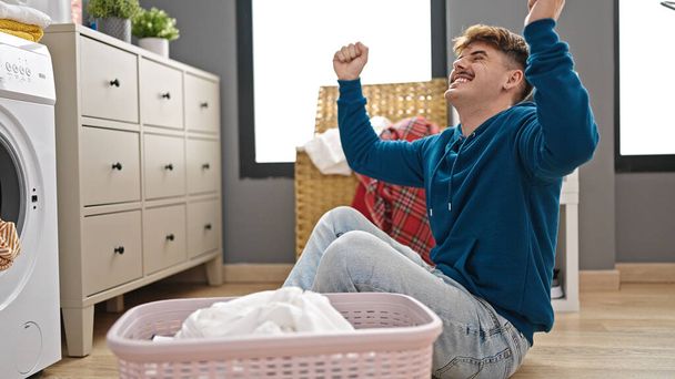 Young hispanic man washing clothes celebrating at laundry room - Photo, Image