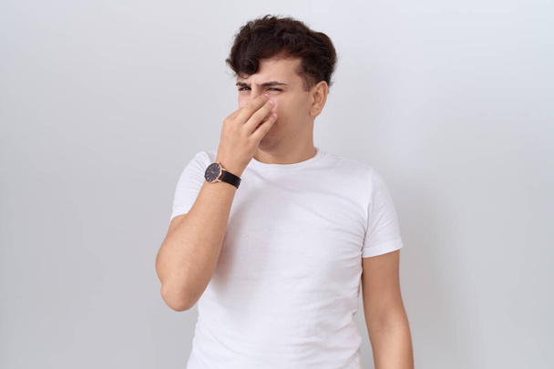 Молодой недвоичный мужчина в обычной белой футболке, пахнущий чем-то вонючим и отвратительным, невыносимым запахом, затаив дыхание пальцами на носу. плохой запах  - Фото, изображение