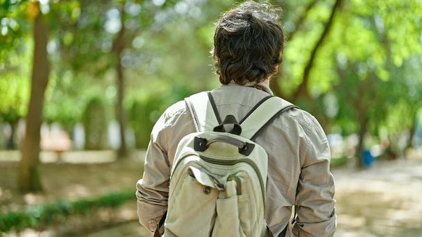 Young hispanic man tourist wearing backpack walking backwards at park - Photo, Image