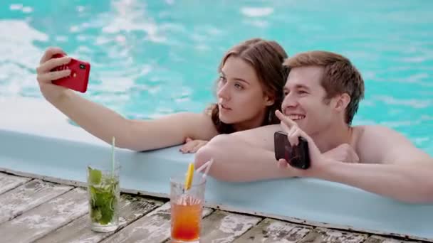 Молодая прекрасная пара фотографируется в отпуске. Два любовника делают селфи вместе в бассейне. Парень и девушка фотографируют свой медовый месяц на курорте. Высококачественные 4k кадры - Кадры, видео