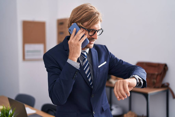 Fiatal szőke férfi üzletember beszél okostelefonon keres óra irodában - Fotó, kép