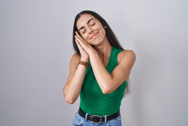 Young woman standing over isolated background sleeping tired dreaming and posing with hands together while smiling with closed eyes.  - Foto, imagen