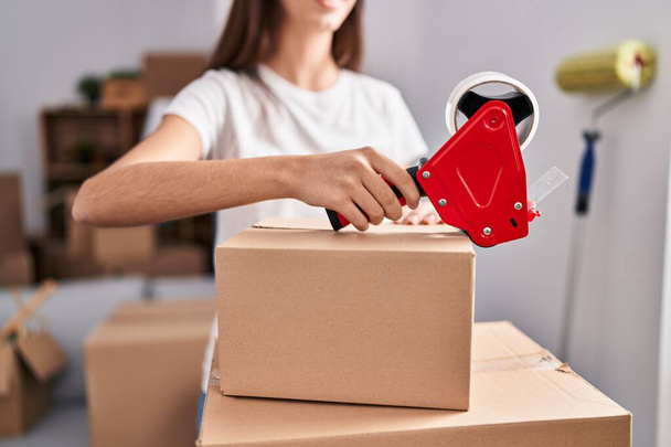 Young beautiful hispanic woman smiling confident packing cardboard box at new home - Photo, Image