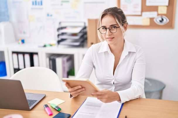Mujer joven rubia trabajadora de negocios leyendo cuaderno en la oficina - Foto, Imagen