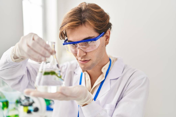 Νεαρός καυκάσιος επιστήμονας που κρατά δοκιμαστικό σωλήνα με φυτό στο εργαστήριο - Φωτογραφία, εικόνα