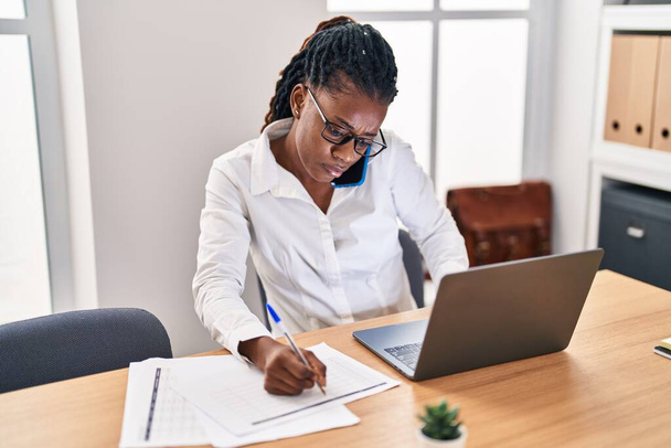 Afrykańska amerykanka pracownik biznesu mówi na smartfonie pisząc na dokumencie w biurze - Zdjęcie, obraz