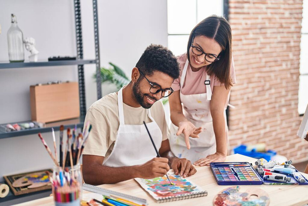 Man and woman artists smiling confident drawing on notebook at art studio - Photo, Image
