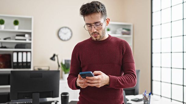 Young hispanic man business worker using smartphone at office - 写真・画像