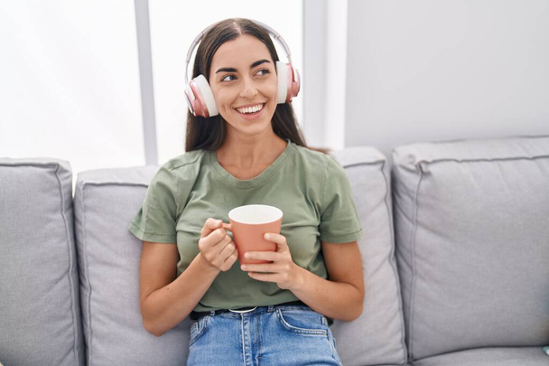 Fiatal, gyönyörű spanyol nő zenét hallgat, kávét iszik otthon. - Fotó, kép