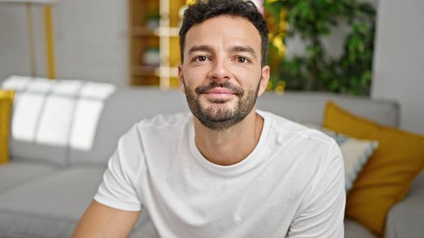 Junger hispanischer Mann lächelt selbstbewusst auf Sofa zu Hause - Foto, Bild