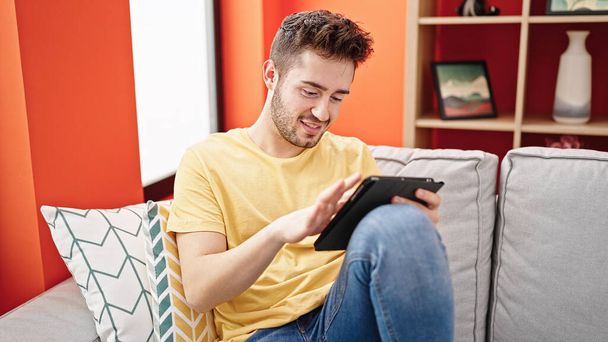 Young hispanic man using touchpad sitting on sofa at home - Photo, Image