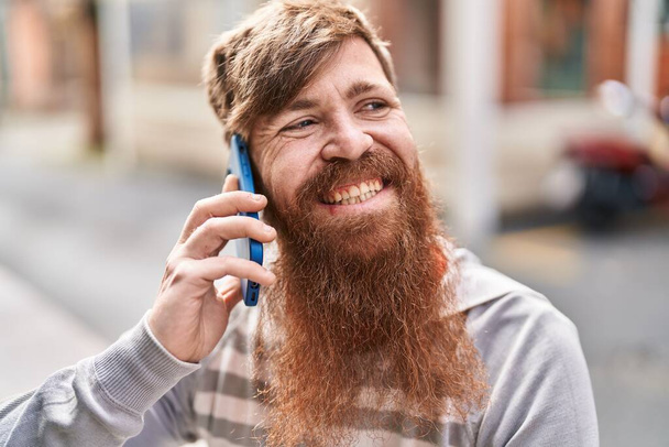 若い赤毛の男は自信を持って話して笑顔路上でスマートフォン - 写真・画像