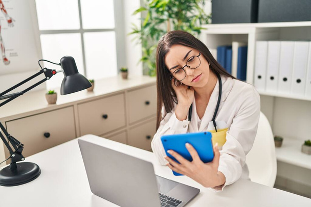 Young beautiful hispanic woman doctor using laptop and touchpad with serious expression at clinic - Fotoğraf, Görsel