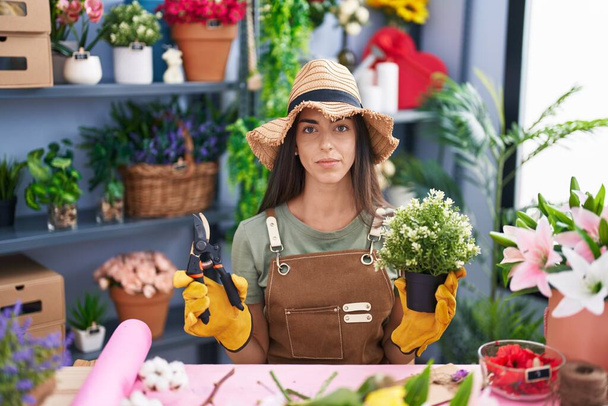 Młoda brunetka pracująca w kwiaciarni zrelaksowana z poważnym wyrazem twarzy. proste i naturalne patrzenie w kamerę.  - Zdjęcie, obraz