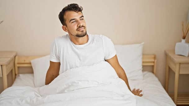Young hispanic man smiling confident sitting on bed at bedroom - Foto, Imagem