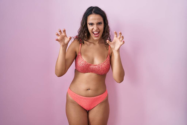 Fiatal spanyol nő visel fehérnemű felett rózsaszín háttér mosolygós vicces csinál karom gesztus mint macska, agresszív és szexi kifejezés  - Fotó, kép