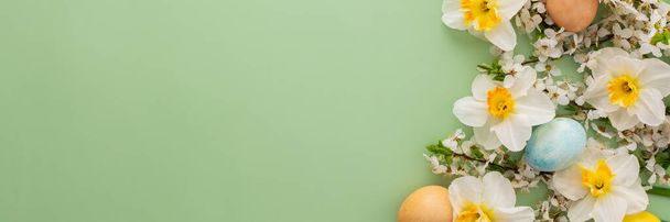 Slavnostní prapor s jarními květy a velikonočními vejci, bílými narcisy a třešňovými větvemi na zeleném pastelovém pozadí - Fotografie, Obrázek